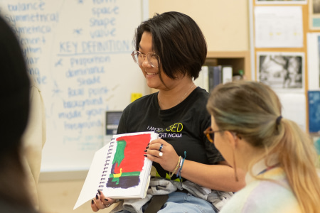 Student smiles while showing off their artwork in AP Art.